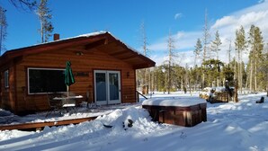 Un chalet en bois doté d’une terrasse, d’un bain à remous et surplombant un paysage enneigé.