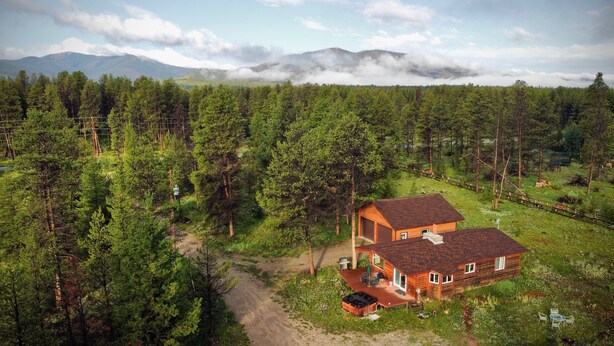 Une cabane en bois avec un toit rouge, entourée d’une forêt dense et avec des montagnes en arrière-plan.