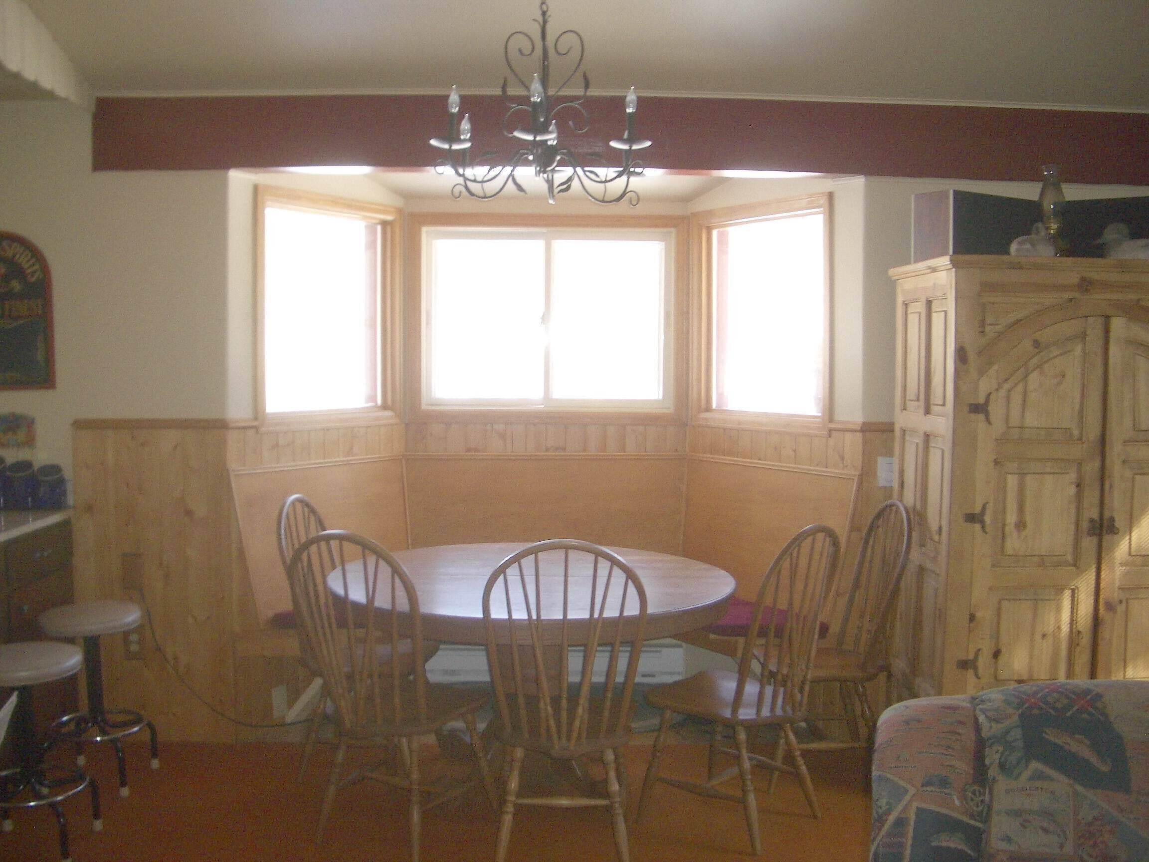 A dining area with a round table and chairs, a chandelier, and a bay window with curtains.