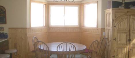 A dining area with a round table and chairs, a chandelier, and a bay window with curtains.