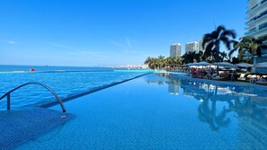 Zona junto a la piscina con vista despejada al océano, sillas de descanso y palmeras.