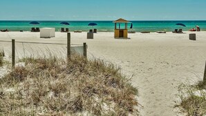 Una playa con una torre de salvavidas, sillas, sombrillas y un sendero de arena.