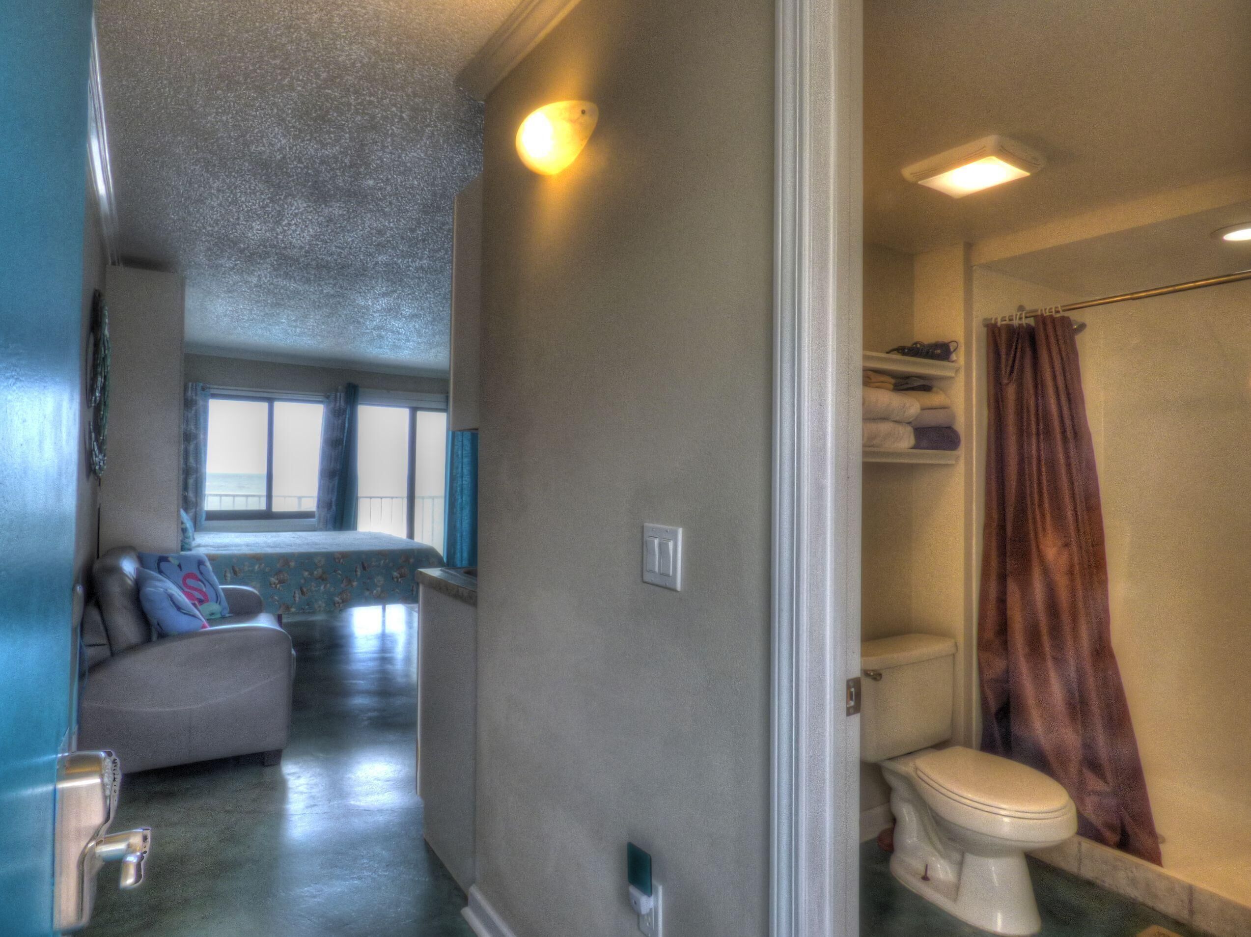 A hallway leading to a bedroom with a bed and a bathroom with a toilet and shower curtain.