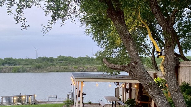 Un espace extérieur abrité, avec une table et des chaises, donnant sur une étendue d’eau.