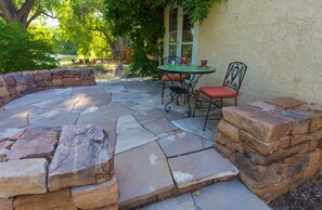A stone patio with a round table and metal chairs, surrounded by a low stone wall. - On the Rio Grande River!!  Rinconada Rio Grande Retreat (Taos)