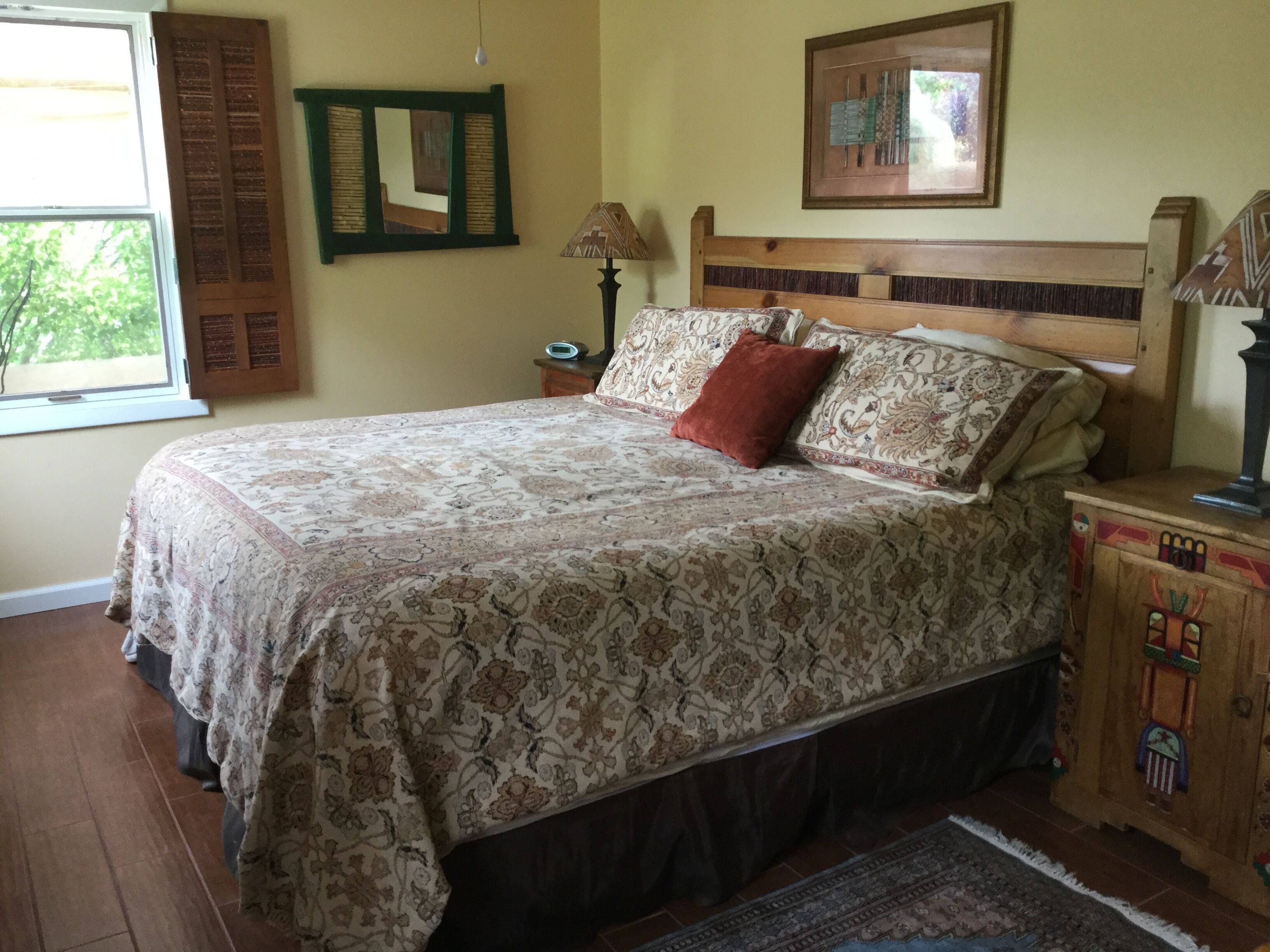 A bedroom with a bed, a nightstand, a lamp, a wooden cabinet, a window with shutters, and a framed picture on the wall.