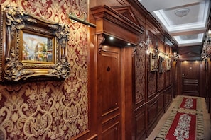 Un pasillo con paneles de madera ornamentados, alfombra roja y un candelabro.
