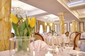 Comedor formal con columnas de mármol, candelabros y mesas dispuestas para una comida.