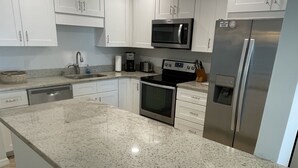 Una cucina con mobili bianchi, un frigorifero in acciaio inossidabile, un forno a microonde, un fornello e una lavastoviglie.