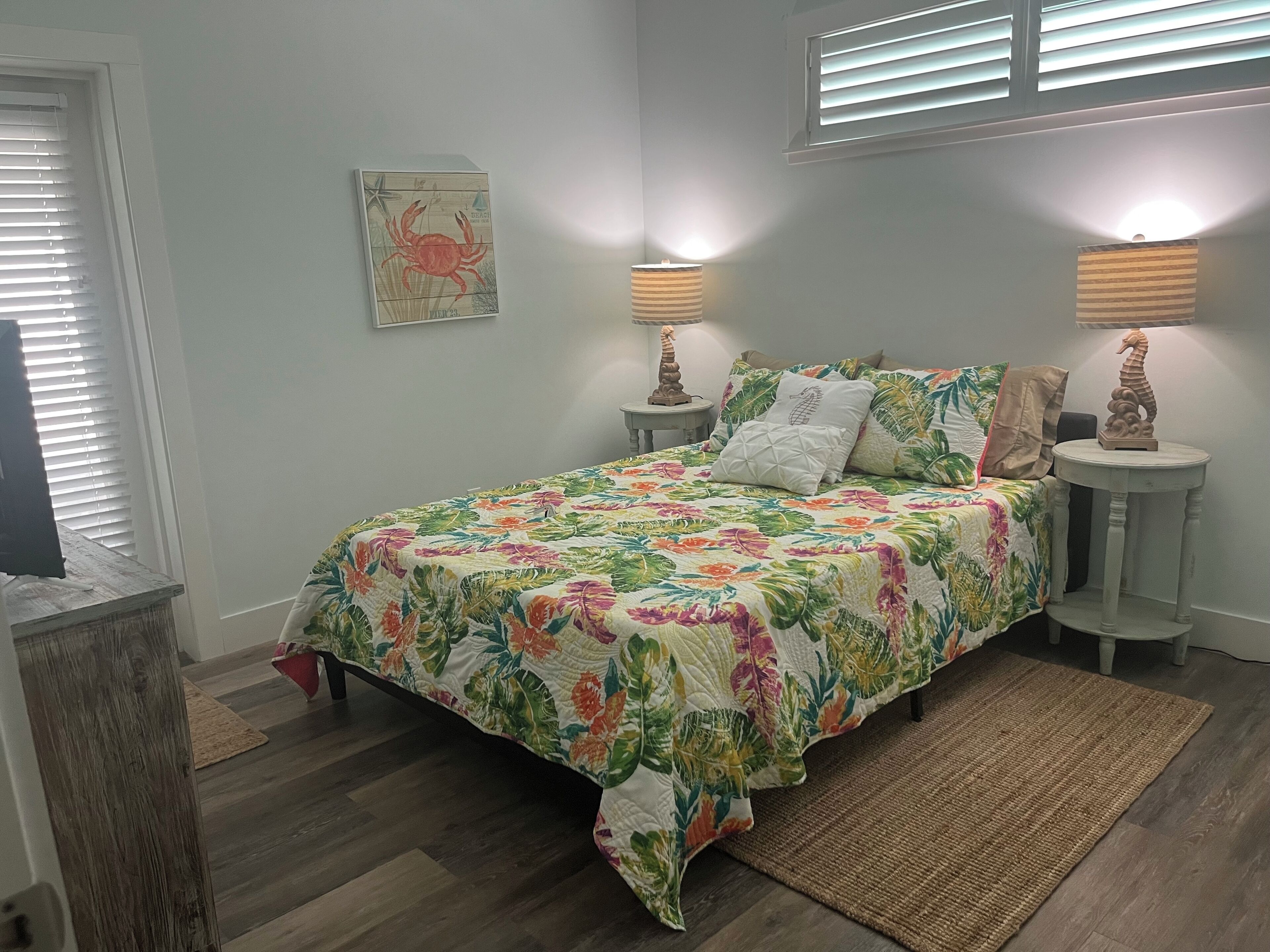 A bedroom with a floral bedspread, two bedside lamps, a seahorse decoration, and a framed picture on the wall.