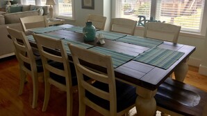 Een eetgedeelte met een houten tafel, witte stoelen en blauwe placemats.