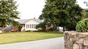 A residential house with a front lawn, a stone wall, and a driveway. - Kingsway Guesthouse. Come, relax, and enjoy your time in Amish country! (Millersburg)