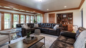 A spacious living room with a large leather sectional sofa, a small round coffee table, and a wooden desk with bookshelves. - Kingsway Guesthouse. Come, relax, and enjoy your time in Amish country! (Millersburg)