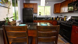 A kitchen with wooden cabinets, a black refrigerator, a stove, and a dining table with chairs. - Secluded garden bungalow in the jungle with air conditioning. (Keaau)