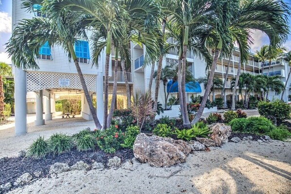 A hotel with a covered outdoor area, palm trees, and a sandy ground.