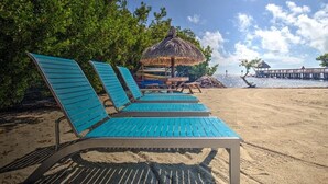 A beach with blue lounge chairs, a thatched umbrella, and a pier in the background. - BLUE / GREEN PARADISE WITH A PRIVATE BEACH!!! (Tavernier)