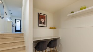 Un intérieur moderne avec un escalier, un bureau blanc avec deux chaises, une œuvre d’art encadrée et une étagère ornée d’objets décoratifs.