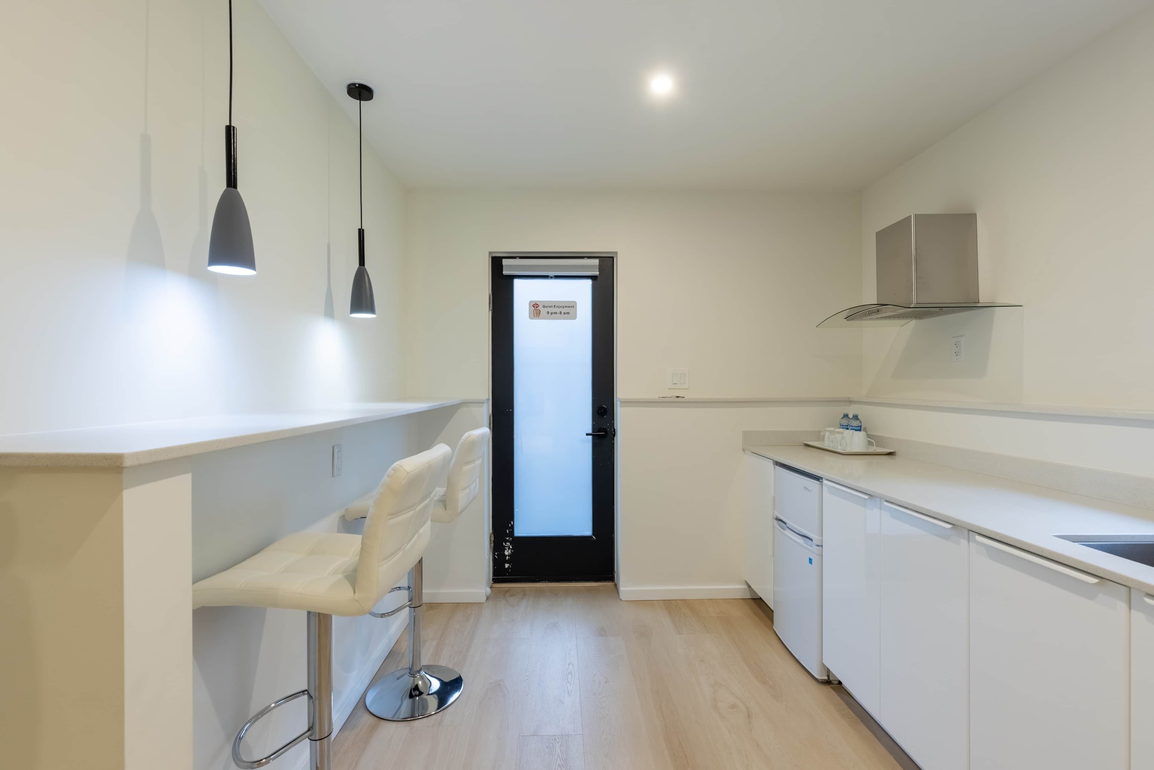 Une cuisine moderne avec des meubles blancs, une porte noire et des luminaires suspendus.