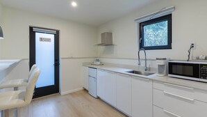 Une cuisine moderne avec des meubles blancs, un four à micro-ondes encastré, une machine à café et une fenêtre donnant sur les arbres.