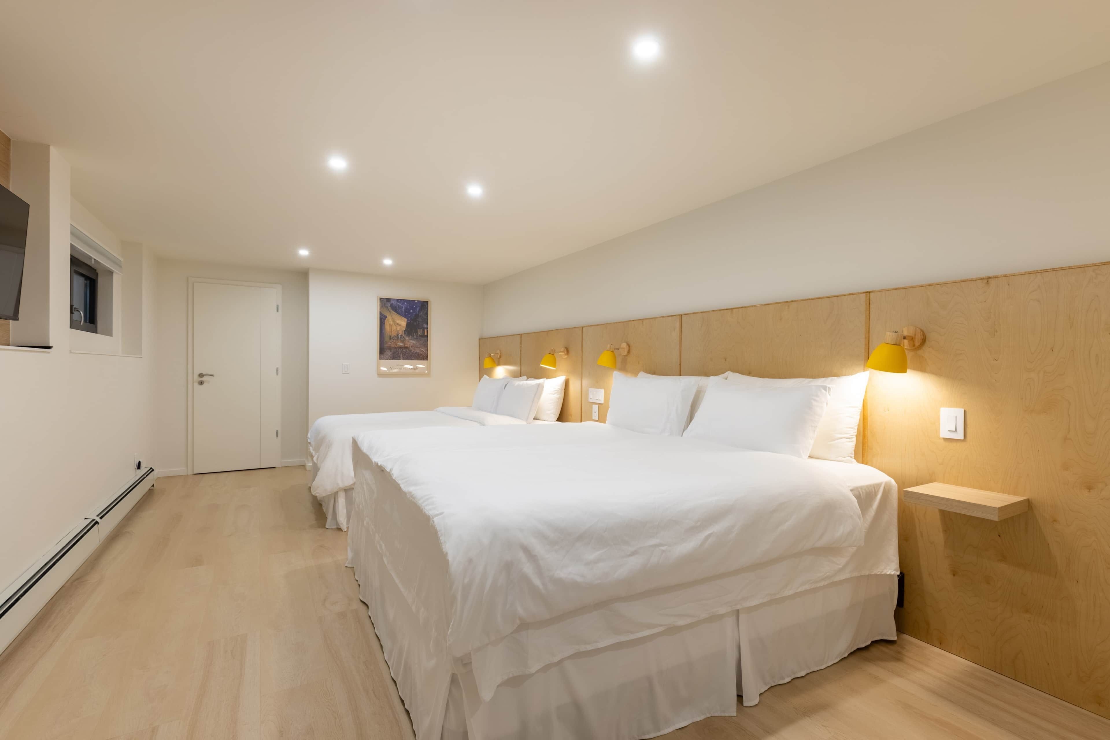 Une chambre à coucher avec une tête de lit en bois, deux lits, des lampes de chevet et une porte blanche.