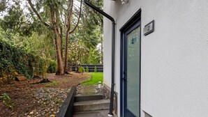 Une maison avec une porte noire, une plaque portant le numéro « 2 », un petit jardin avec un chemin de pierres et un arbre.