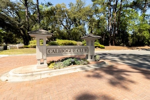 A sign for Calibogue Club with a brick pathway and trees in the background.