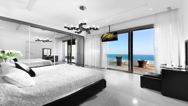 A modern bedroom with a large bed, a TV, and a balcony with a view of the sea. - Luxury 5-Bedroom Oceanfront Penthouse with Private Pool (Bat Yam)