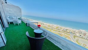 A balcony with a green artificial turf, a wicker chair, and a small table with a vase of flowers. - Luxury 5-Bedroom Oceanfront Penthouse with Private Pool (Bat Yam)