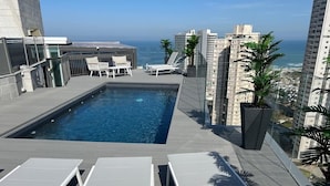 A rooftop pool with lounge chairs, a small seating area, and a view of the ocean and cityscape. - Luxury 5-Bedroom Oceanfront Penthouse with Private Pool (Bat Yam)