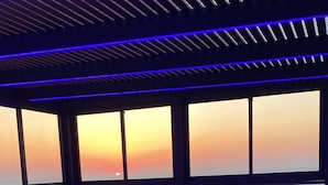 A modern lounge area with a view of the sunset over the water, featuring comfortable seating and a potted plant. - Luxury 5-Bedroom Oceanfront Penthouse with Private Pool (Bat Yam)