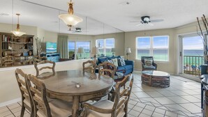 A spacious living area with a large dining table, comfortable seating, and a balcony with a view. - Top Floor Gulf View + Pet Friendly • Free Daily Beach Service (Destin)