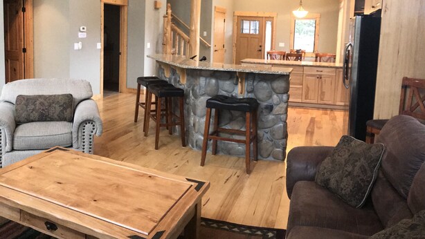 Amplia sala de estar con techo alto, escalera de madera y cocina con isla de piedra.