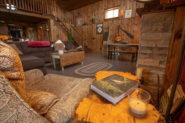 A cozy living room with a sofa, a coffee table with a book and candle, and a staircase leading to another level.