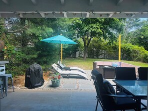 Een overdekt terras met buitenmeubilair, een barbecue en uitzicht op de achtertuin.