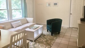 Een woonkamer met een witte bank, een blauwgroene fauteuil, een salontafel en een plafondventilator.