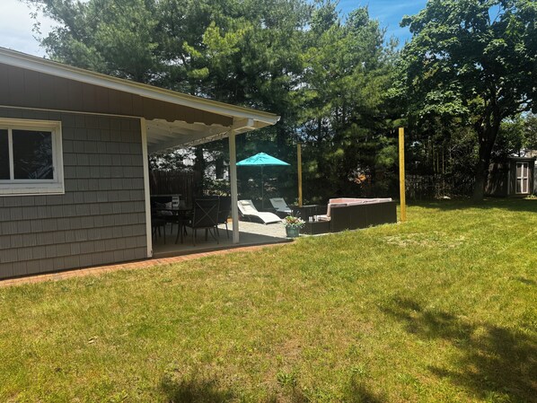 A covered patio with a table and chairs, a small shed, and a grassy yard.