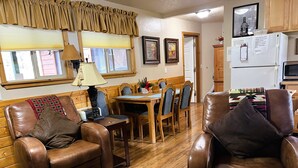 Una sala de estar acogedora con sofás de cuero, una mesa de comedor y una zona de cocina con refrigerador y microondas.