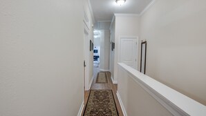 A narrow hallway with a patterned rug, white walls, and a door at the end. - Gwinnett St Row: Historic 3 BR 2BA - Balcony - Free St Parking - Near Forsyth Pk (Savannah)