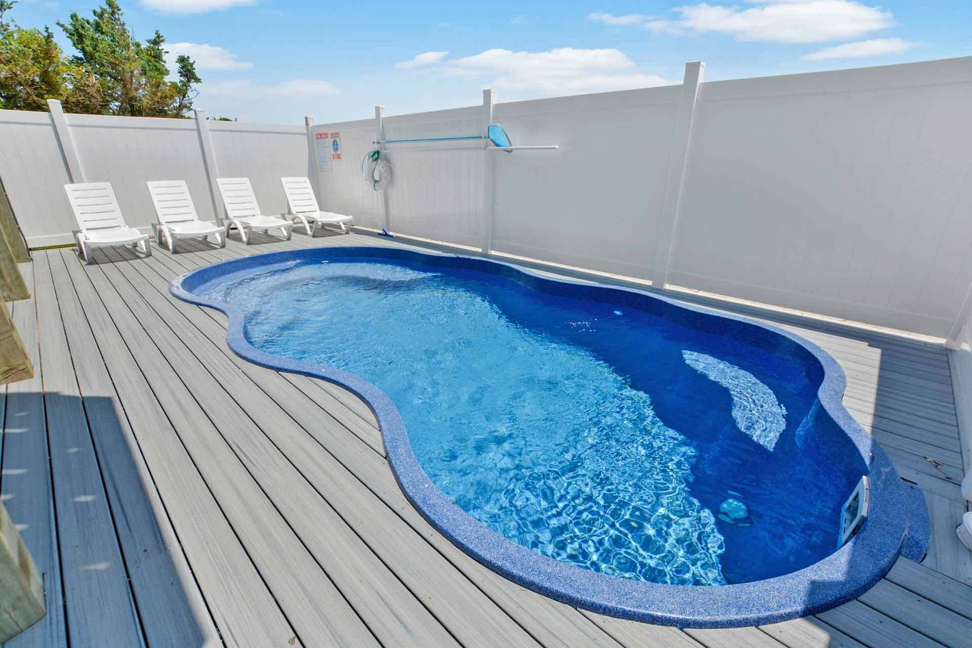 A swimming pool with a wooden deck, surrounded by white walls and a blue sky.