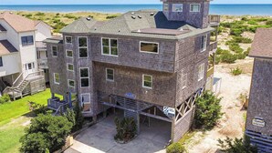 A multi-story building with a beach view, a small tower-like structure on the roof, and a sign indicating a surf sound. - Oceanfront Dog Friendly Home with Pool, Hot Tub, EV Charger, and Home Theater (Salvo)