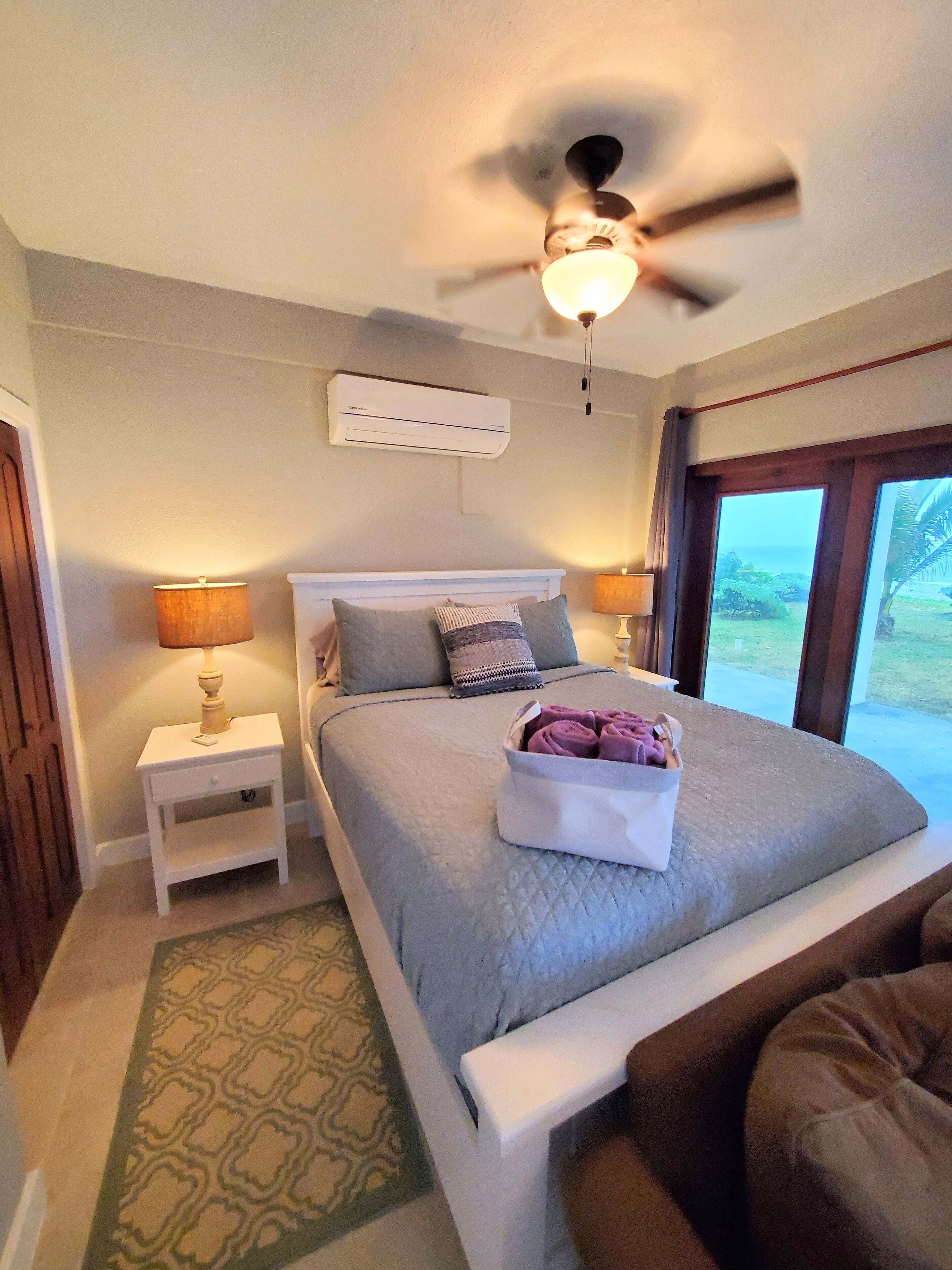 Une chambre à coucher avec un lit, des tables de chevet, un ventilateur de plafond et une vue par la fenêtre.