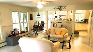 Un vaste espace de vie comprenant un canapé, une table basse en verre et une table à manger avec des chaises. On aperçoit également un coin cuisine avec des placards et un comptoir, situés à l’arrière-plan.