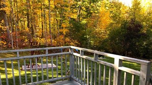 Une terrasse en bois, dotée d’une balustrade, surplombe une zone herbeuse parsemée d’arbres aux feuilles d’automne aux couleurs flamboyantes.