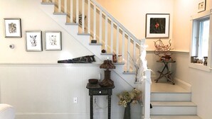 Un escalier avec une rampe blanche, une petite table sur laquelle est posé un vase de fleurs et des œuvres d’art encadrées accrochées aux murs.