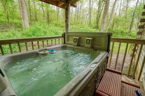 A hot tub with a wooden deck and a forest backdrop. - Blue Rose Cabins - Oleander Cabin (Logan)