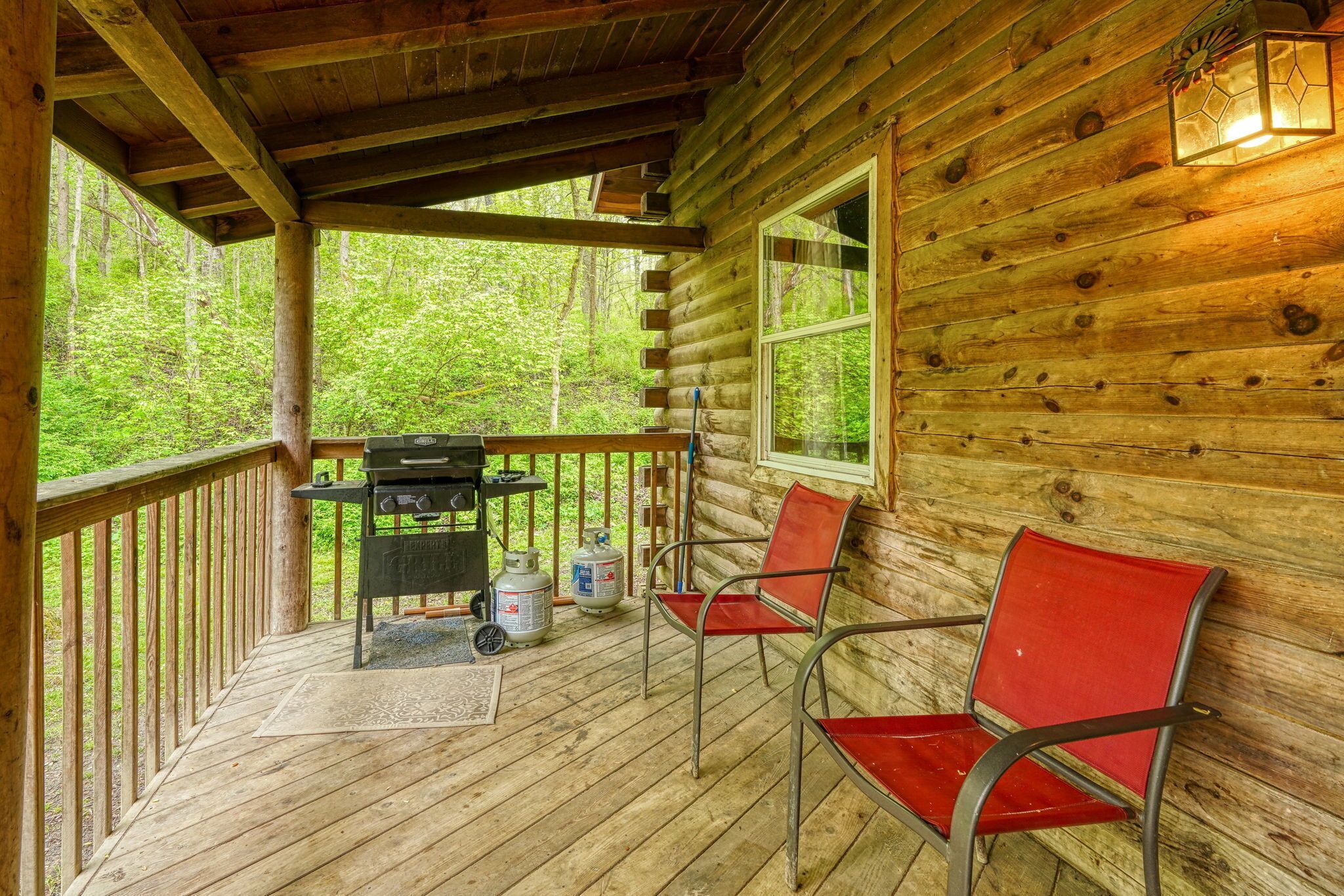 Une cabane en bois avec un porche couvert, un barbecue, deux chaises et des bouteilles de propane.