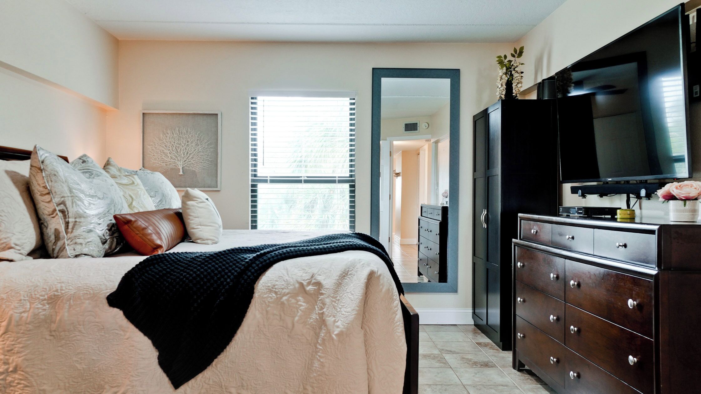 A bedroom with a bed, dresser, TV, and a window with blinds.