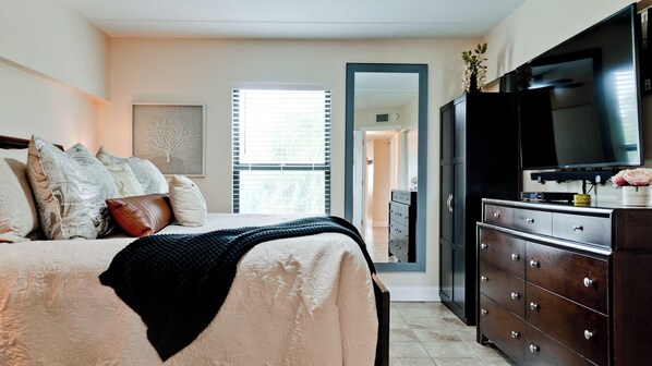 A bedroom with a bed, dresser, TV, and a window with blinds.