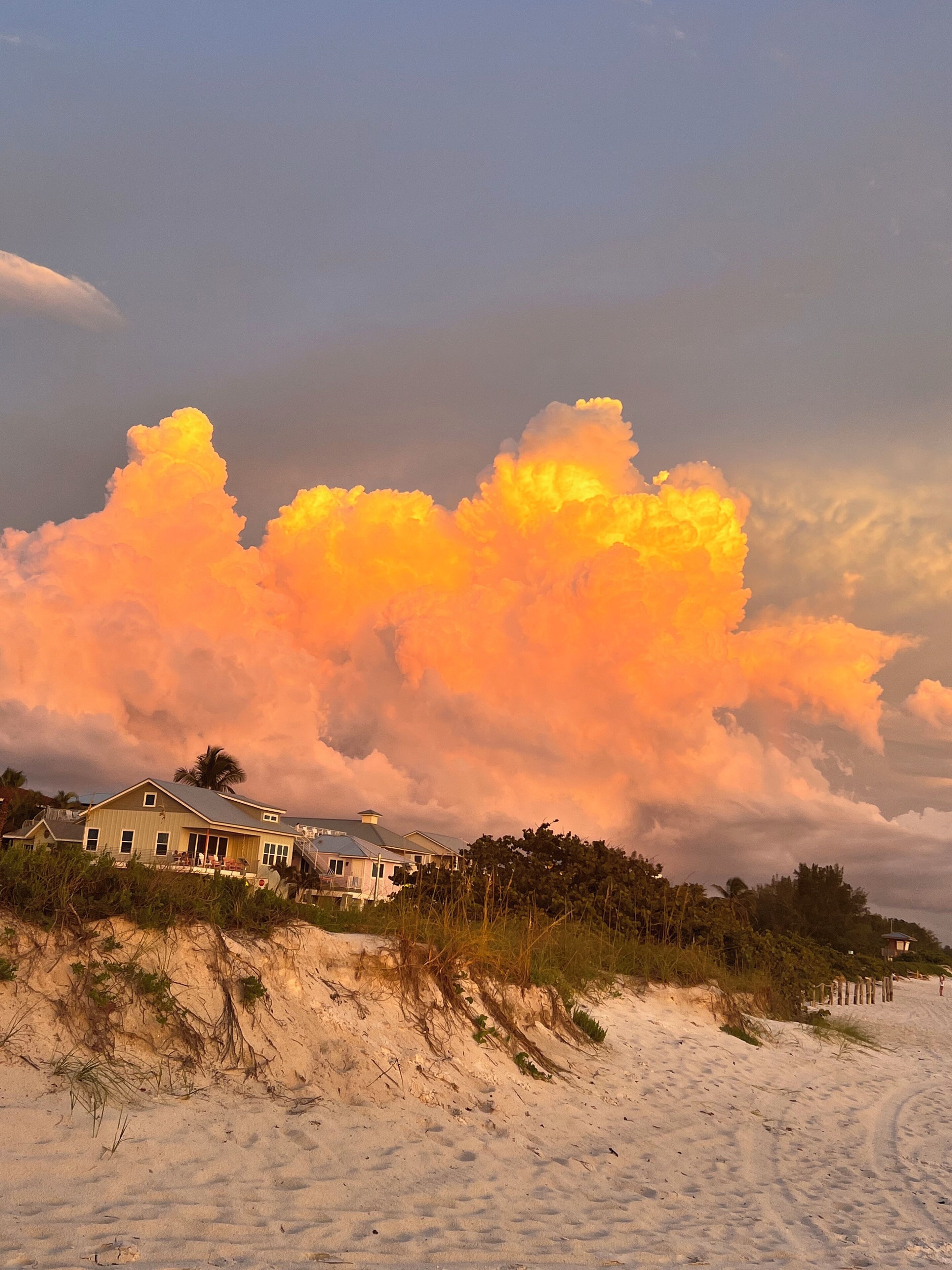 Une propriété située en bord de mer, avec une grande maison, des dunes de sable et un ciel nuageux.