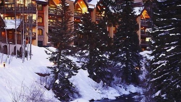 Eine Lodge mit mehreren Gebäuden, einem mit Schnee bedeckten Bachlauf und umliegenden Nadelbäumen.